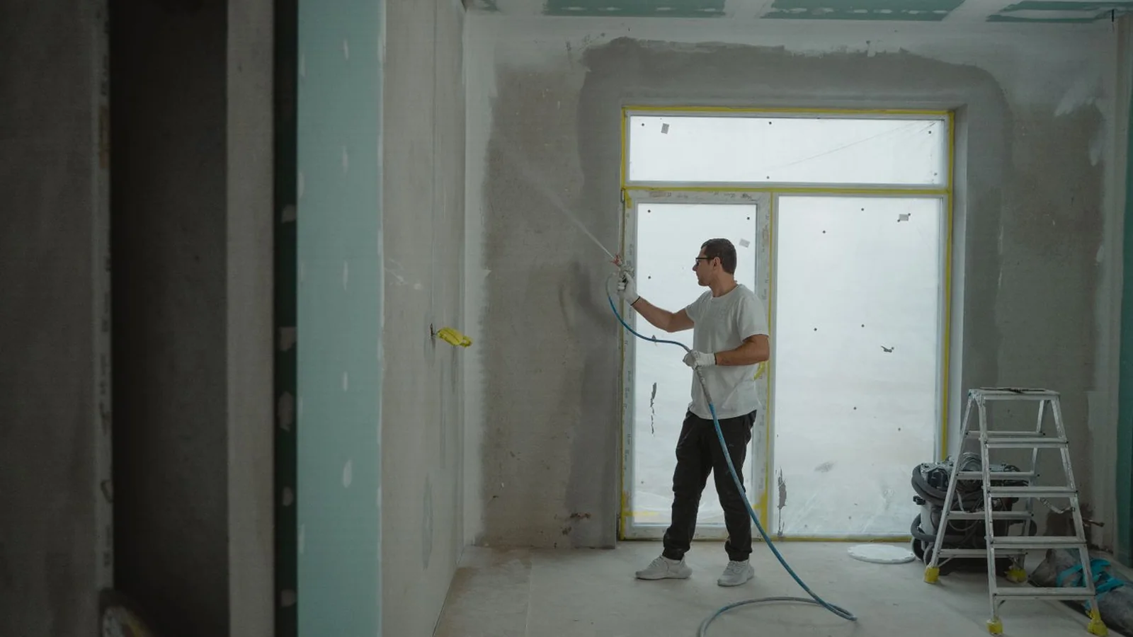 Profesional aplicando pintura con pistola en el interior de una vivienda en reforma